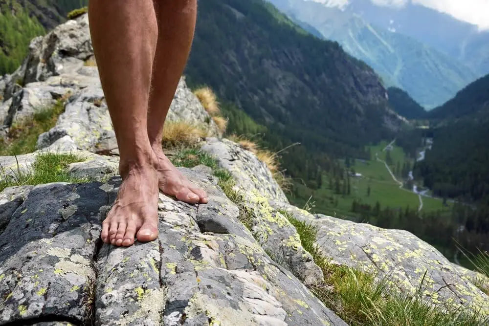 Barefoot hiker standing on rocky mountain edge, illustrating need for grip toe socks with five-toe design