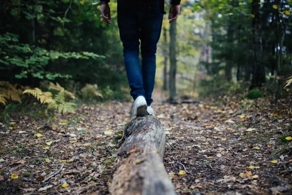 Person walking along a log in forest trail, symbolizing balance, natural movement, and foot stability