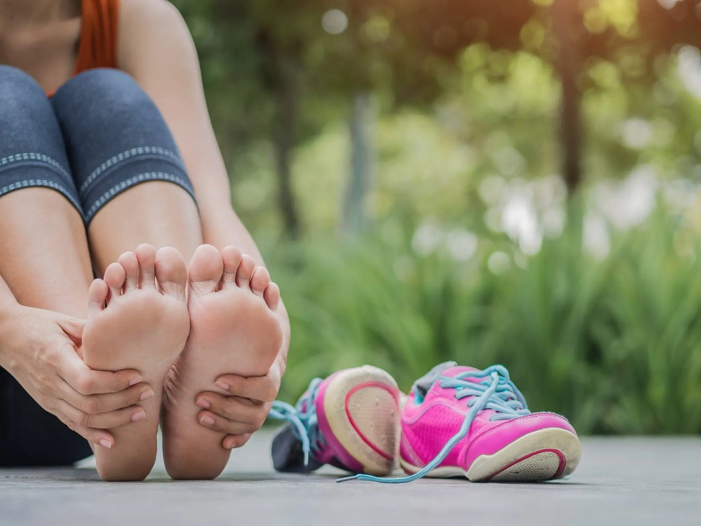 Woman sitting barefoot after exercise, holding sore feet with running shoes nearby, illustrating tingling feet in pregnancy