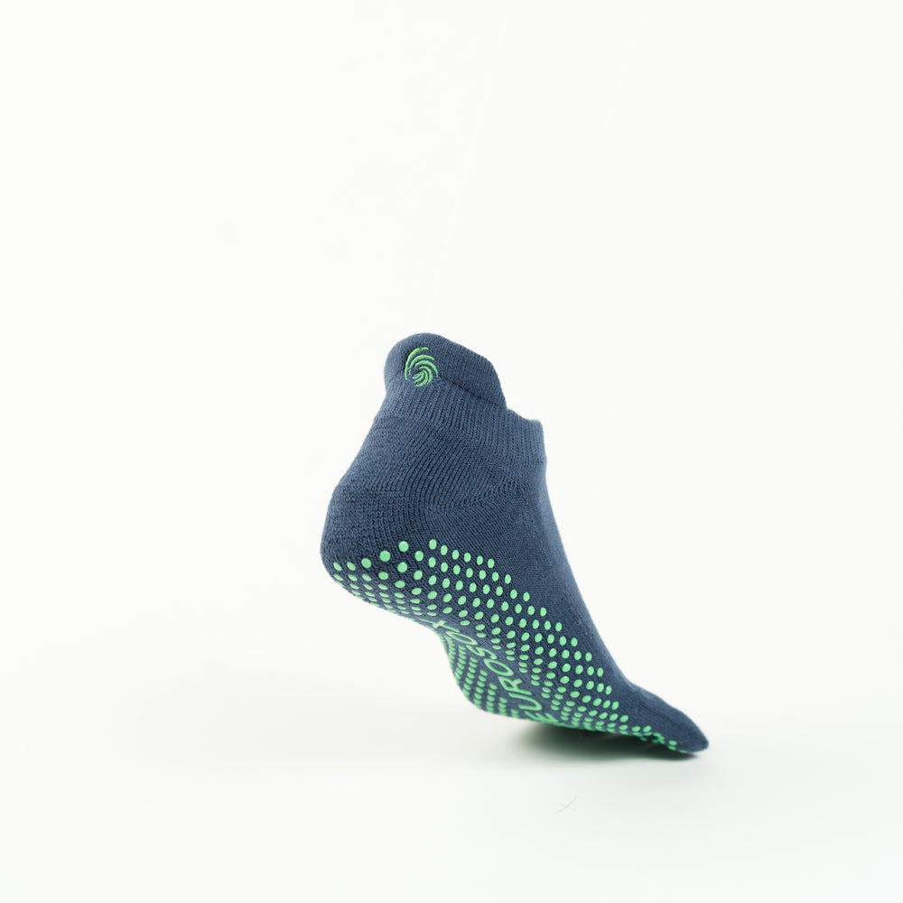 The image shows a single navy colored sock with green grip dots on the sole, positioned as if suspended in mid-air against a plain white background. The sock has a small green swirl logo near the ankle area.