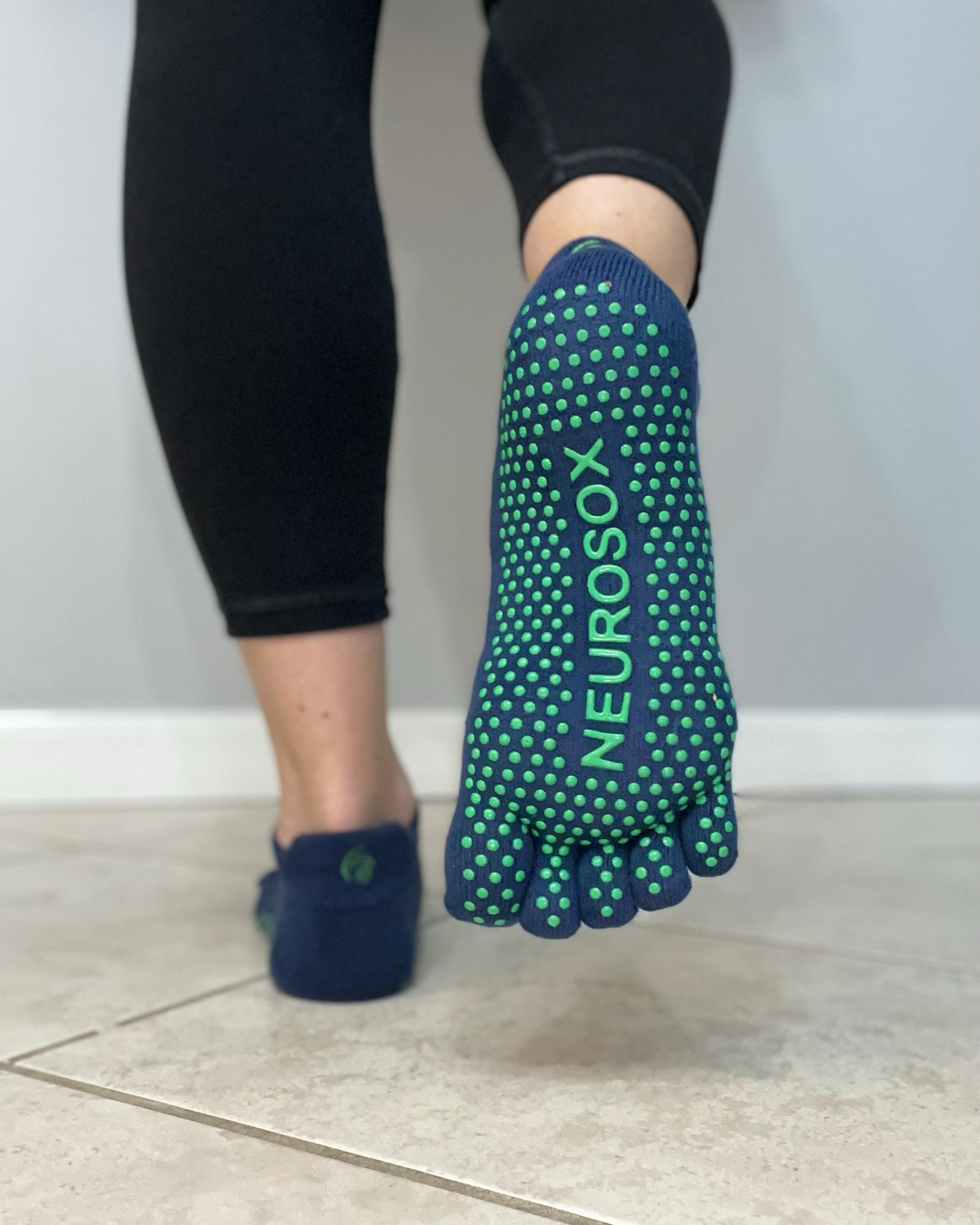 
                  
                    Person wearing blue and green NeuroSox grip toe socks while standing on a tile floor, showcasing non-slip sole design
                  
                