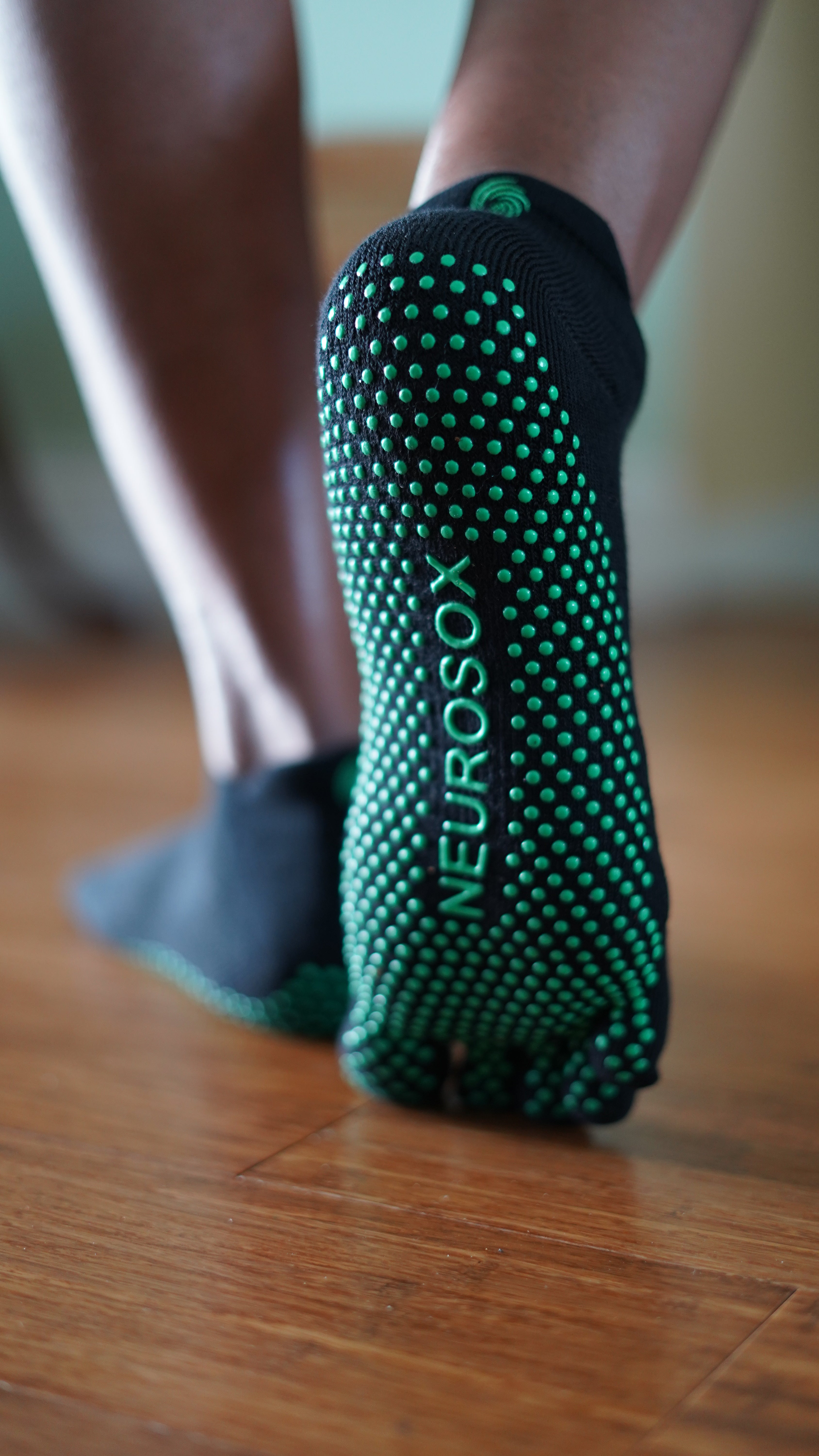 Close-up of NeuroSox Five Toe Grip Sock sole with green anti-slip grip and brand logo on hardwood floor