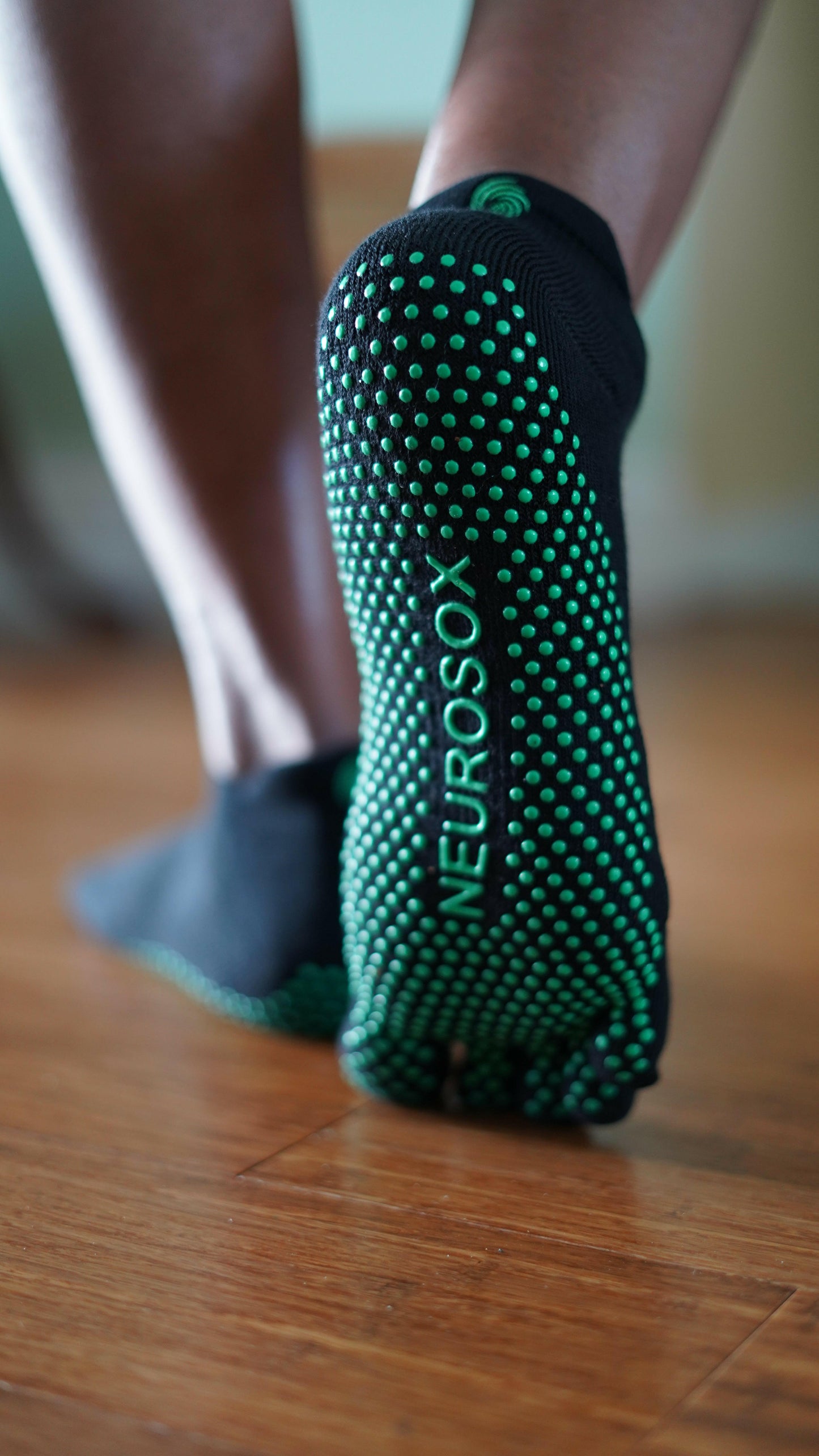 
                  
                    Close-up of NeuroSox Five Toe Grip Sock sole with green anti-slip grip and brand logo on hardwood floor
                  
                