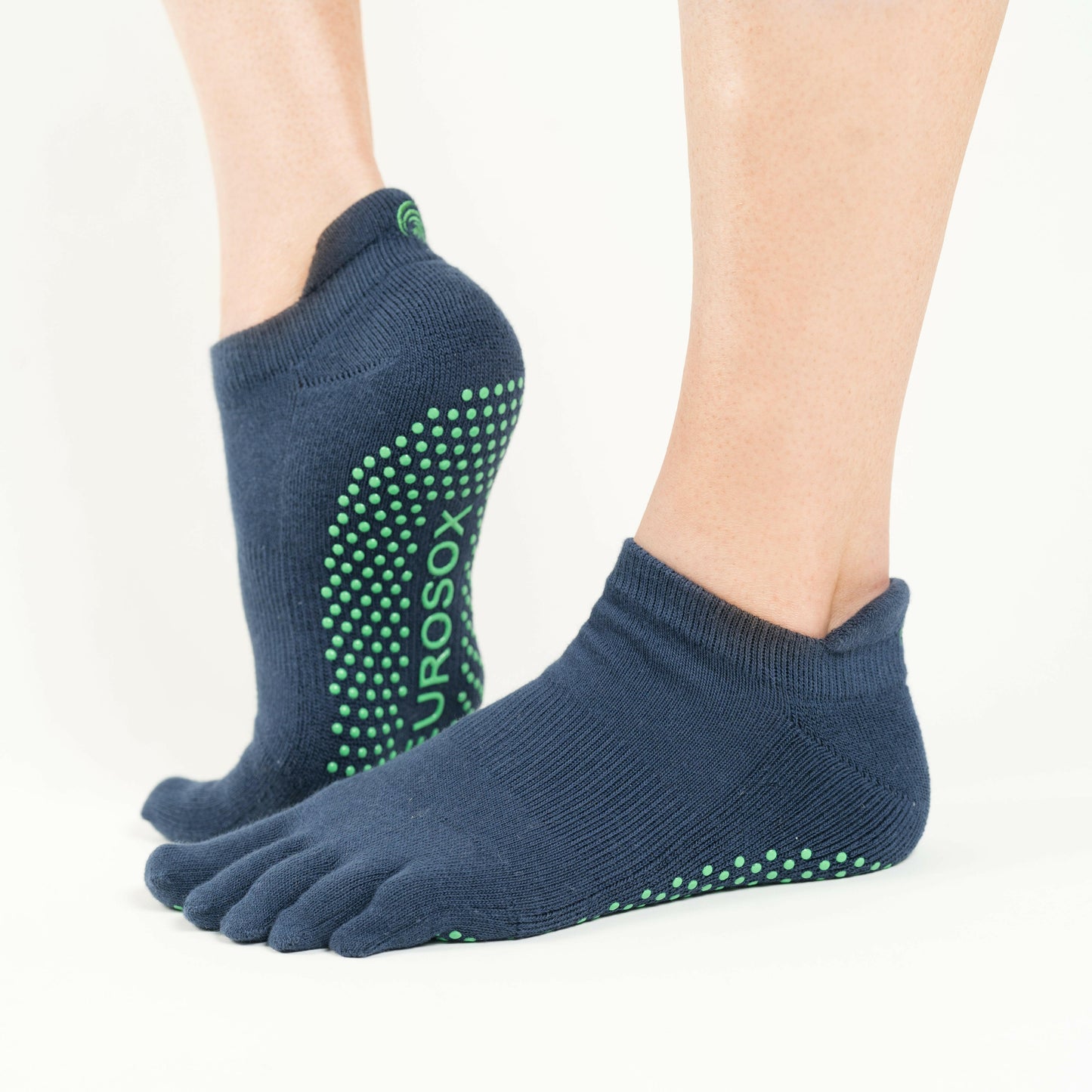 Navy blue NeuroSox Five Toe Grip Socks on feet with green anti-slip sole, shown in standing position.